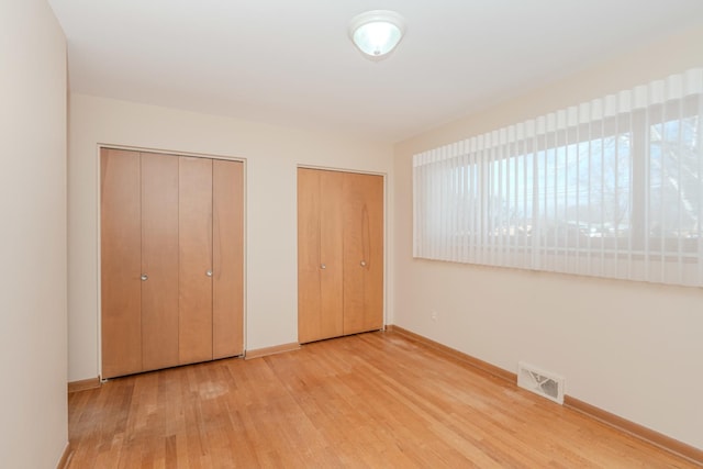 unfurnished bedroom featuring baseboards, visible vents, multiple closets, and wood finished floors