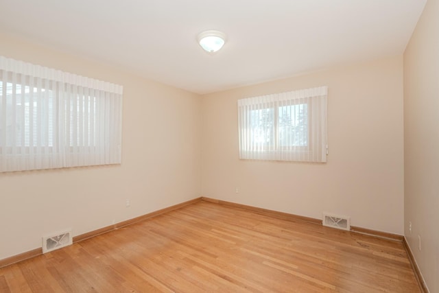 empty room with light wood-type flooring, visible vents, and baseboards