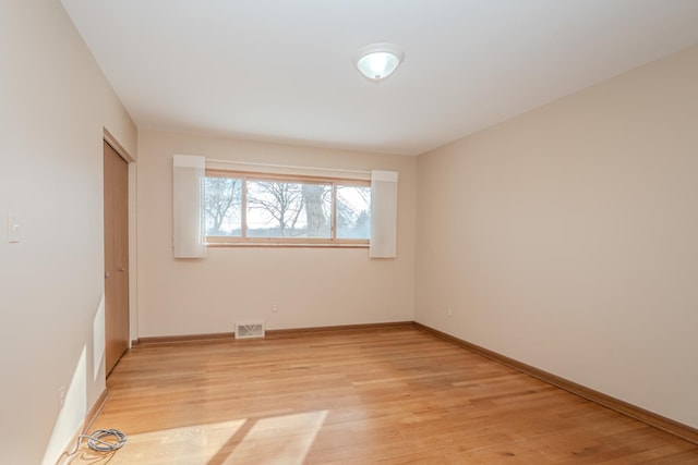 empty room featuring light wood-type flooring, visible vents, and baseboards