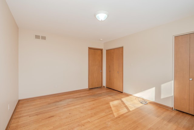 empty room featuring wood finished floors, visible vents, and baseboards