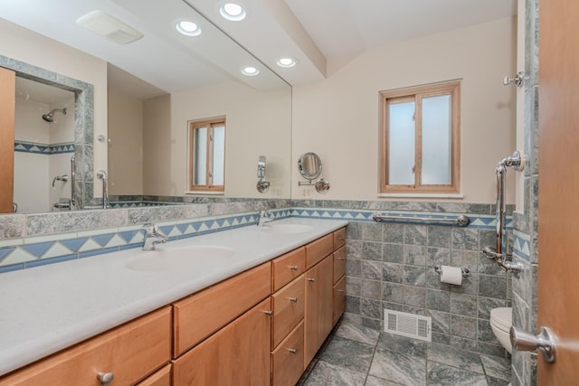 bathroom featuring toilet, double vanity, a sink, and visible vents