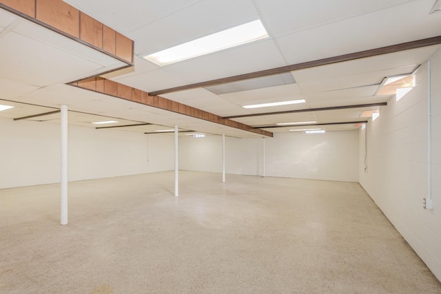 finished basement featuring a paneled ceiling and concrete block wall