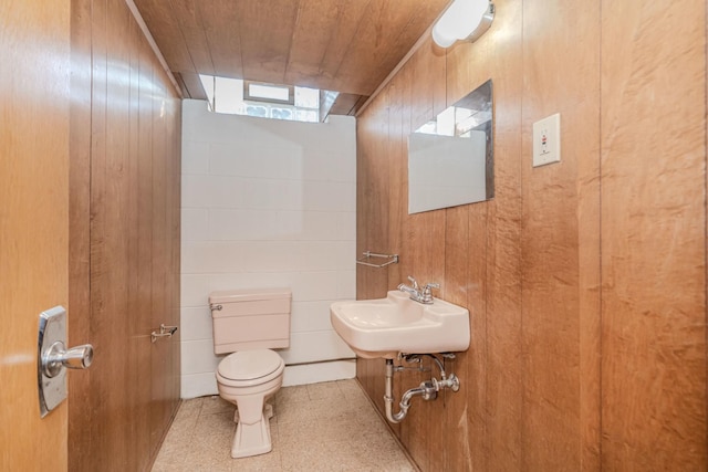 half bathroom with wood ceiling, a sink, wood walls, and toilet