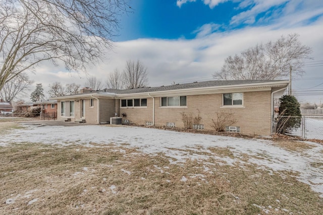 snow covered back of property with a chimney, fence, central AC, and brick siding