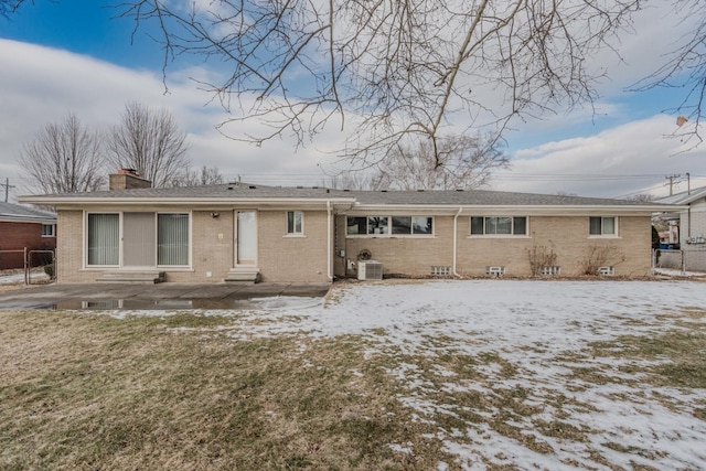 snow covered rear of property with entry steps, a chimney, fence, and brick siding