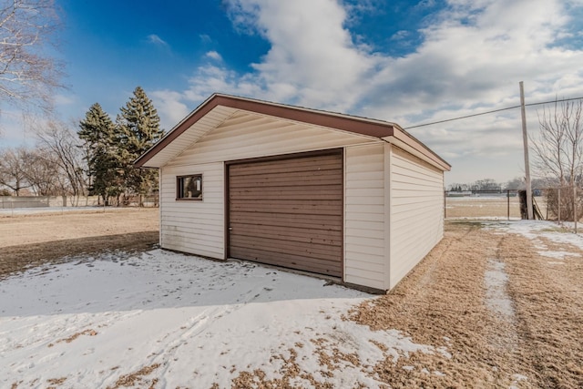 snow covered garage featuring a garage and fence