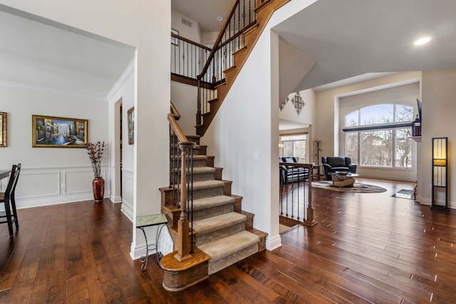 staircase featuring wood-type flooring, a high ceiling, and visible vents