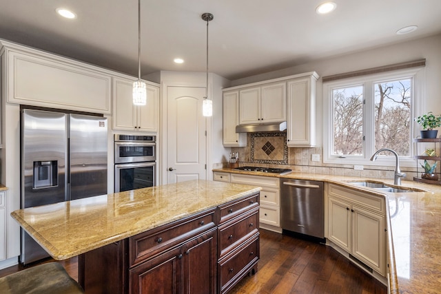 kitchen with decorative backsplash, light stone counters, stainless steel appliances, under cabinet range hood, and a sink