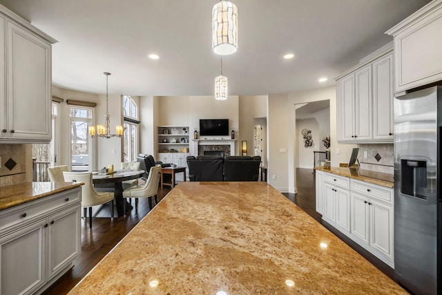 kitchen featuring tasteful backsplash, stainless steel fridge, dark wood finished floors, light stone countertops, and a fireplace