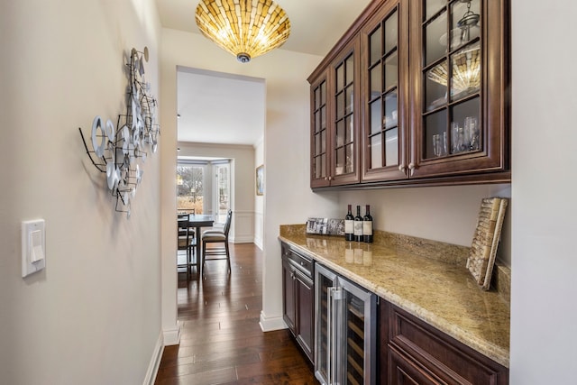 bar with beverage cooler, baseboards, dark wood finished floors, a bar, and a notable chandelier