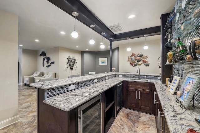 kitchen featuring light stone counters, dark brown cabinetry, beverage cooler, a peninsula, and a sink