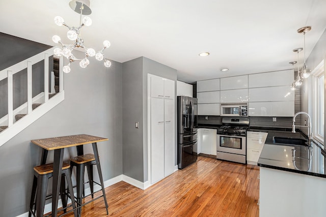 kitchen featuring sink, light hardwood / wood-style flooring, white cabinetry, stainless steel appliances, and decorative light fixtures