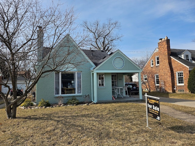 view of front of home with brick siding, covered porch, a chimney, and a front yard