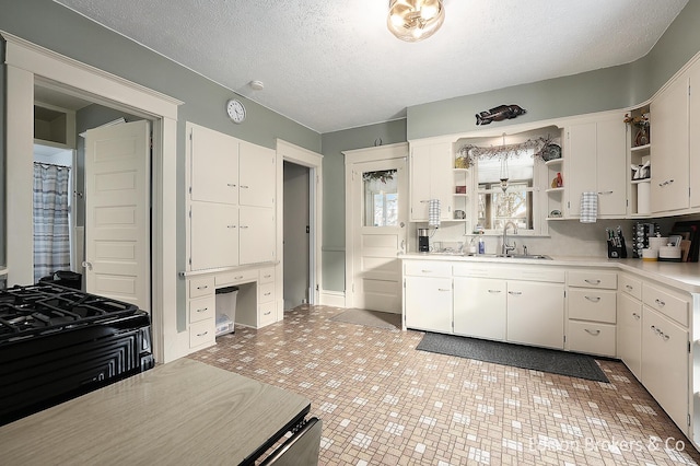 kitchen featuring sink, a textured ceiling, built in desk, and white cabinets