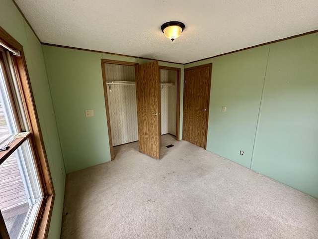 unfurnished bedroom featuring light carpet, multiple windows, ornamental molding, and a textured ceiling