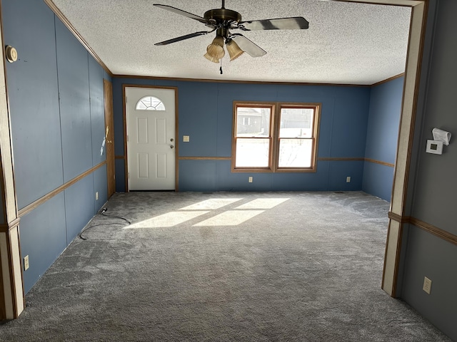 carpeted entrance foyer with ceiling fan, ornamental molding, and a textured ceiling