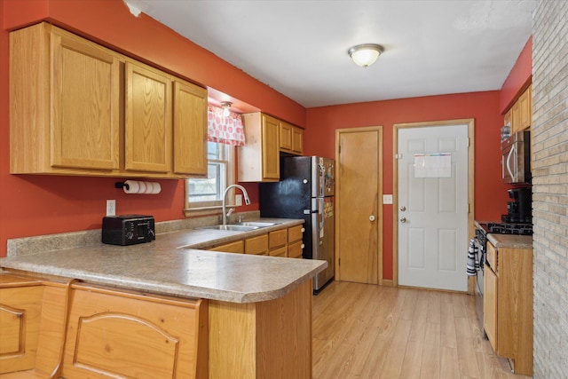 kitchen with appliances with stainless steel finishes, sink, light wood-type flooring, and kitchen peninsula