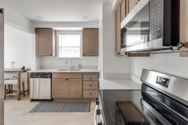 kitchen with appliances with stainless steel finishes, sink, and light hardwood / wood-style flooring