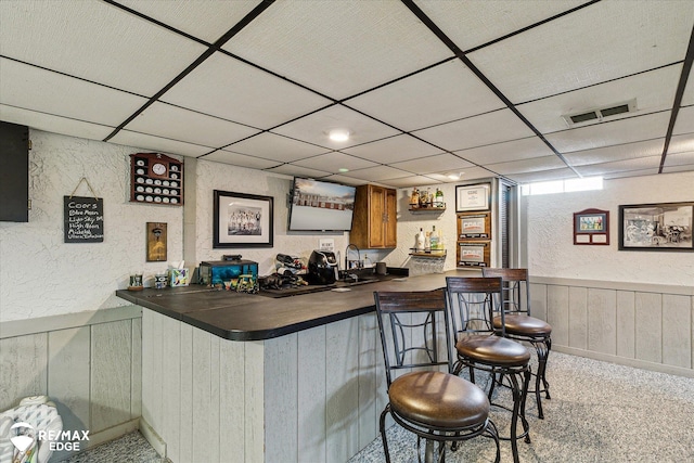 bar with a drop ceiling, wooden walls, and light carpet