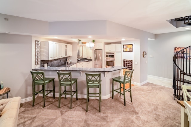 kitchen with white cabinetry, kitchen peninsula, stainless steel appliances, a kitchen bar, and decorative backsplash