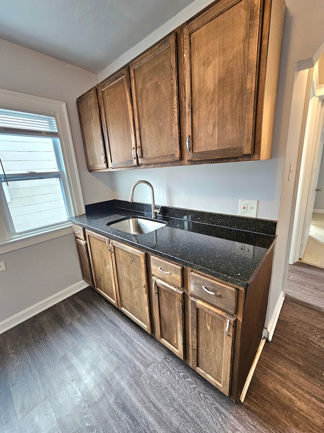 kitchen with dark wood-type flooring, dark stone counters, dishwasher, and sink