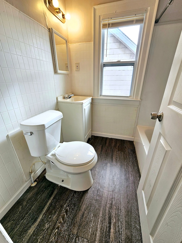 bathroom featuring tile walls, a tub to relax in, hardwood / wood-style flooring, vanity, and toilet