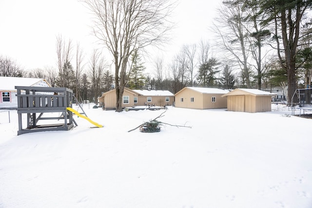 snowy yard featuring a trampoline, a playground, and a shed