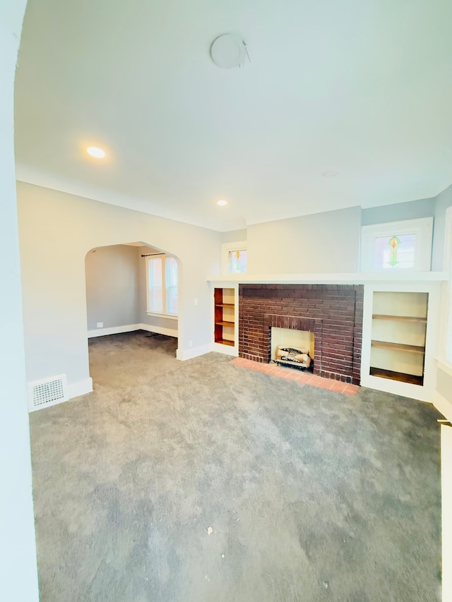 unfurnished living room featuring a brick fireplace, carpet flooring, and built in shelves