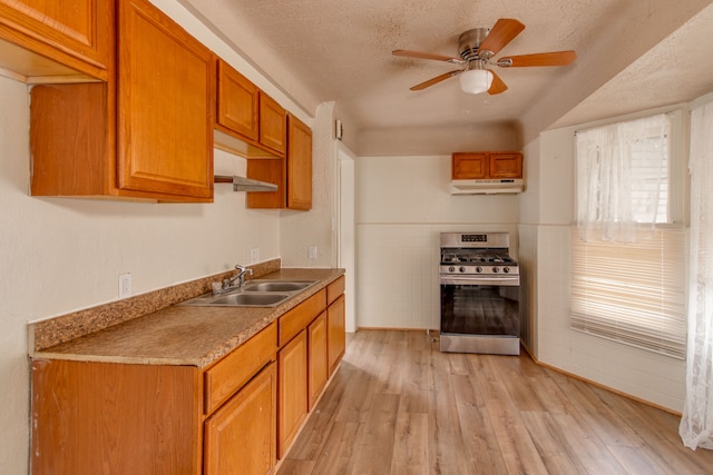 kitchen featuring sink, stainless steel gas stove, a textured ceiling, ceiling fan, and light hardwood / wood-style floors