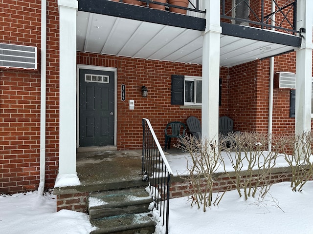 snow covered property entrance with brick siding and a porch