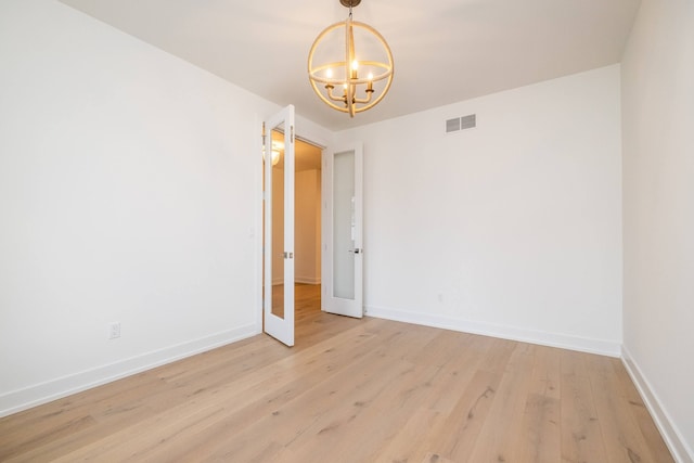 spare room with visible vents, light wood finished floors, baseboards, and a notable chandelier