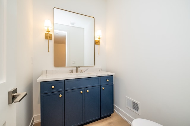 half bath featuring toilet, baseboards, visible vents, wood finished floors, and vanity