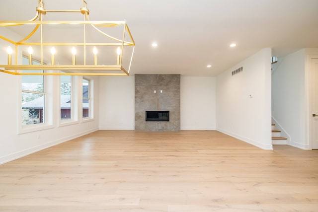 unfurnished living room featuring baseboards, light wood-style flooring, visible vents, and stairway