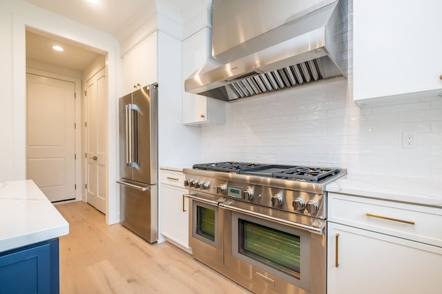 kitchen with wall chimney exhaust hood, light wood-style flooring, white cabinets, and premium appliances