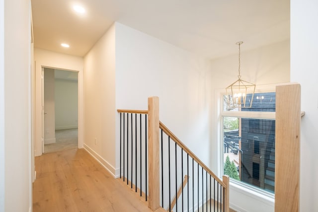 hallway featuring light wood finished floors, baseboards, recessed lighting, an upstairs landing, and a notable chandelier