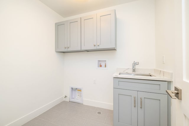 washroom featuring a sink, baseboards, hookup for a washing machine, cabinet space, and light tile patterned floors