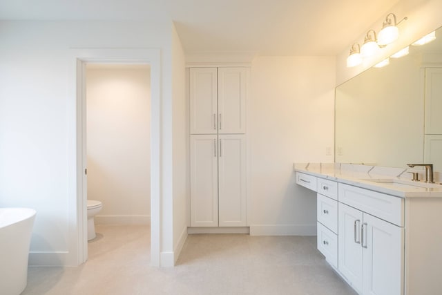 bathroom with toilet, a freestanding tub, vanity, and baseboards