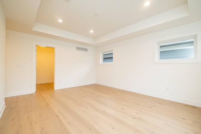 empty room with baseboards, a tray ceiling, visible vents, and light wood-type flooring