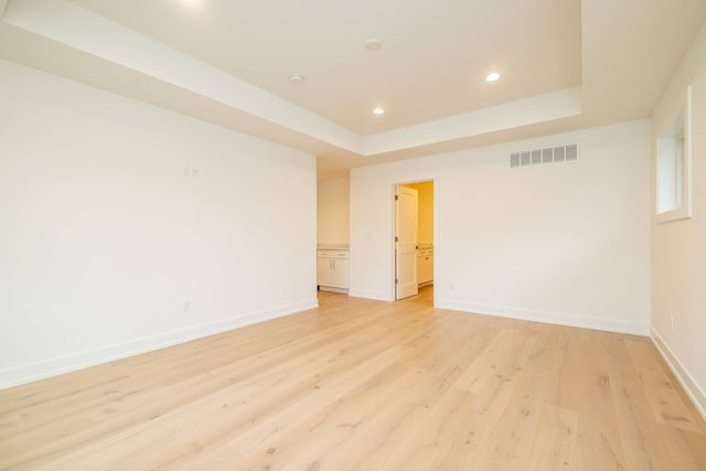 unfurnished room featuring light wood finished floors, a raised ceiling, baseboards, visible vents, and recessed lighting