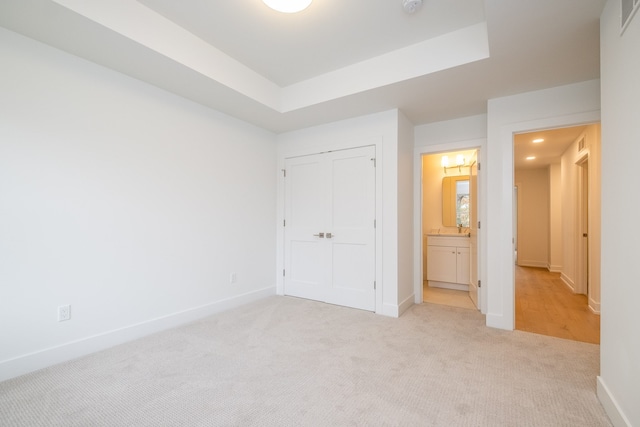 unfurnished bedroom with a closet, light colored carpet, and a tray ceiling