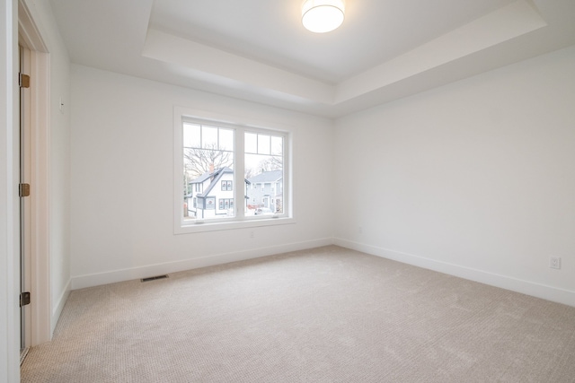 empty room featuring light colored carpet, baseboards, a tray ceiling, and visible vents