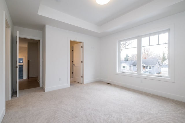 unfurnished bedroom with a raised ceiling, baseboards, visible vents, and light colored carpet