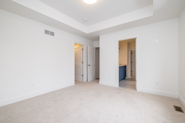 unfurnished bedroom featuring connected bathroom, a tray ceiling, and light carpet