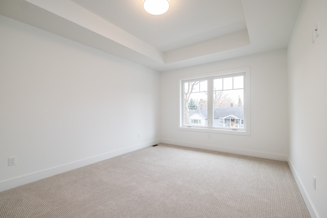spare room with a tray ceiling, baseboards, and light colored carpet