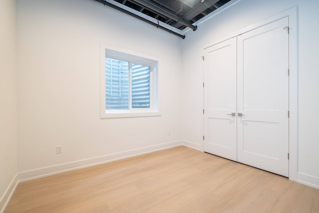 unfurnished bedroom featuring light wood-style flooring, baseboards, and a closet