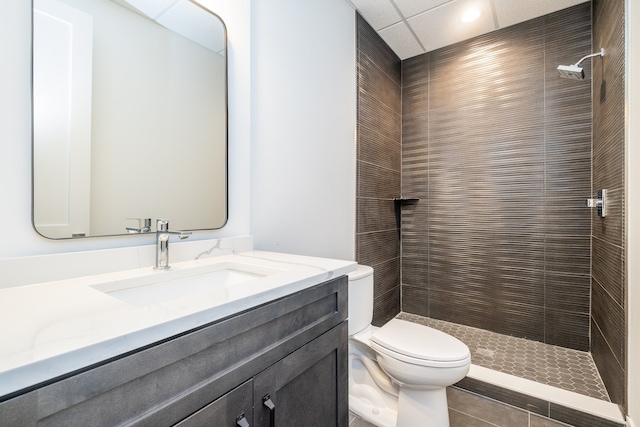 bathroom featuring tile patterned flooring, a tile shower, toilet, and vanity