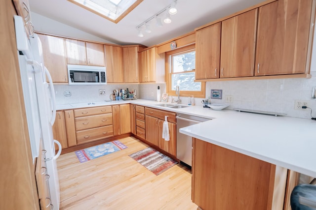 kitchen featuring sink, appliances with stainless steel finishes, backsplash, lofted ceiling with skylight, and light hardwood / wood-style floors