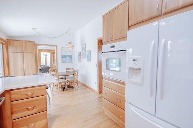 kitchen with light brown cabinetry, lofted ceiling, hanging light fixtures, light hardwood / wood-style floors, and white appliances