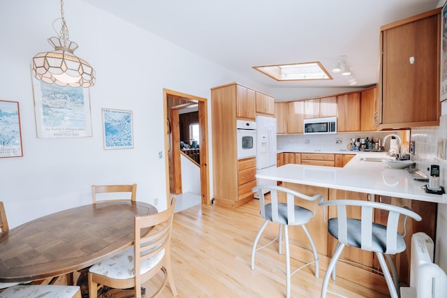 kitchen featuring sink, white appliances, a skylight, decorative light fixtures, and kitchen peninsula