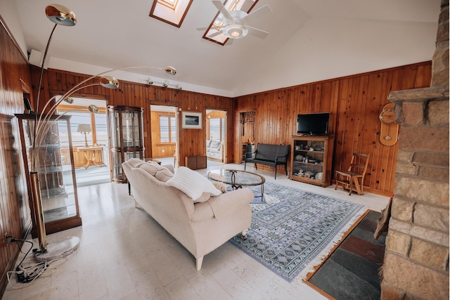 living room with ceiling fan, high vaulted ceiling, wooden walls, and a skylight